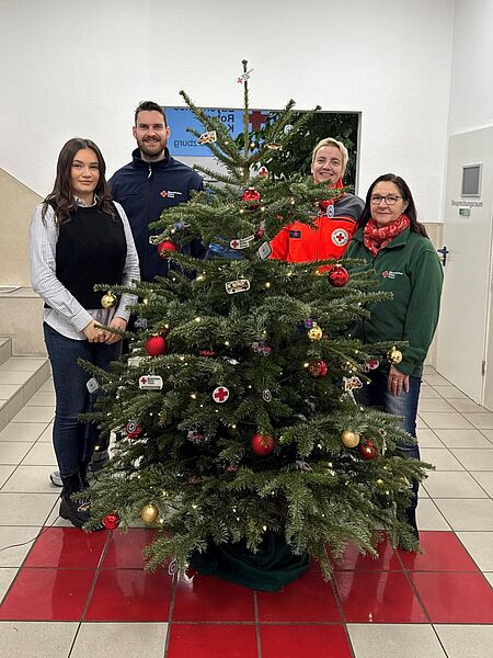 Vier Mitarbeitende des BRK stehen um einen geschmückten Weihnachtsbaum